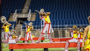 Musicians perform on elevated red platforms in matching striped uniforms at night.