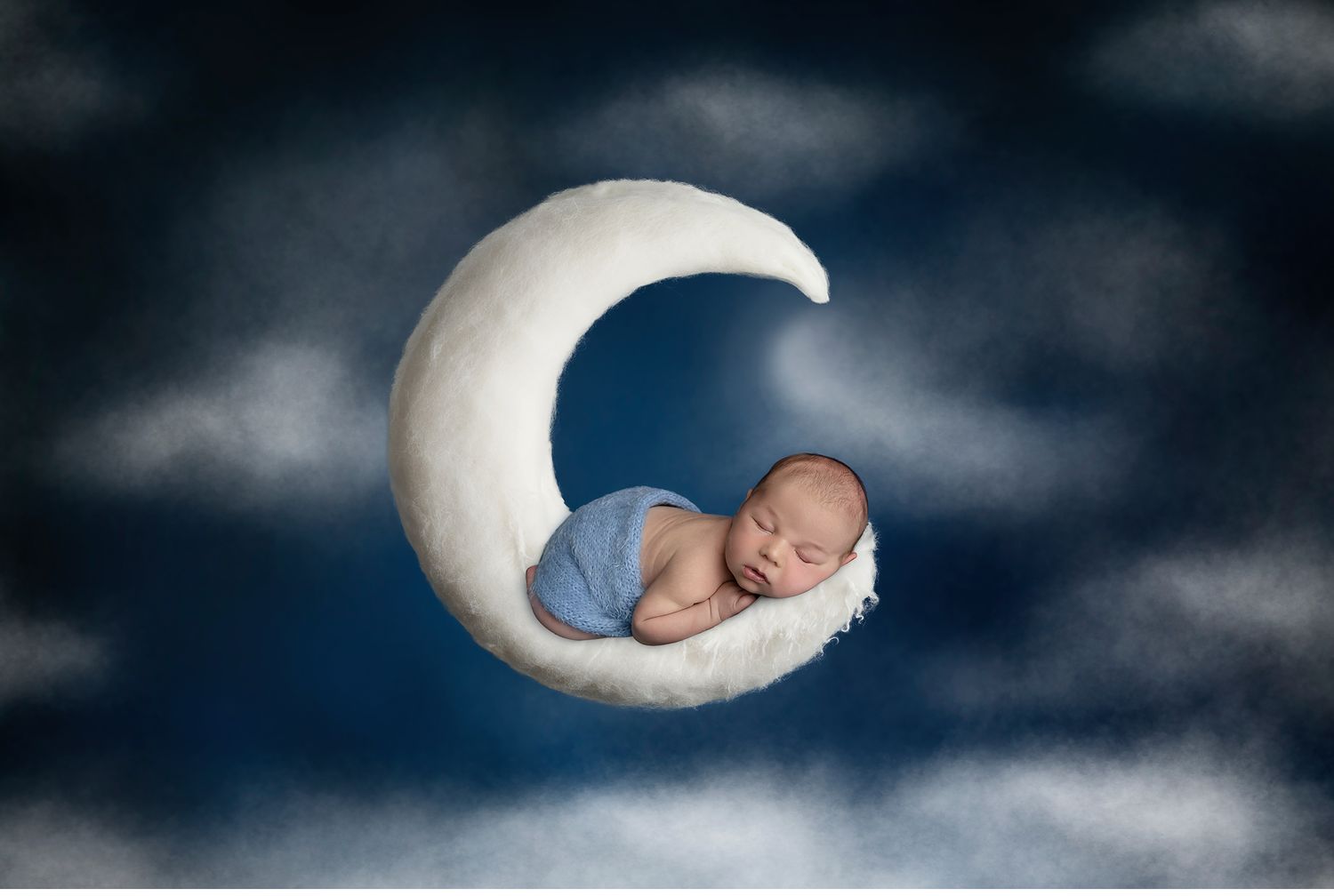 Sleeping newborn baby posed on crescent moon prop with cloudy sky backdrop in Austin studio