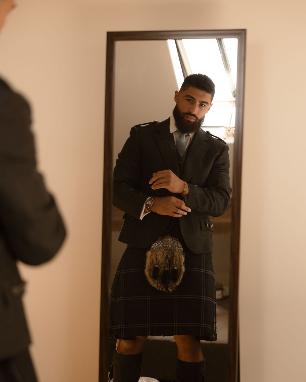 A person takes a mirror selfie wearing a black traditional kilt and matching formal jacket.