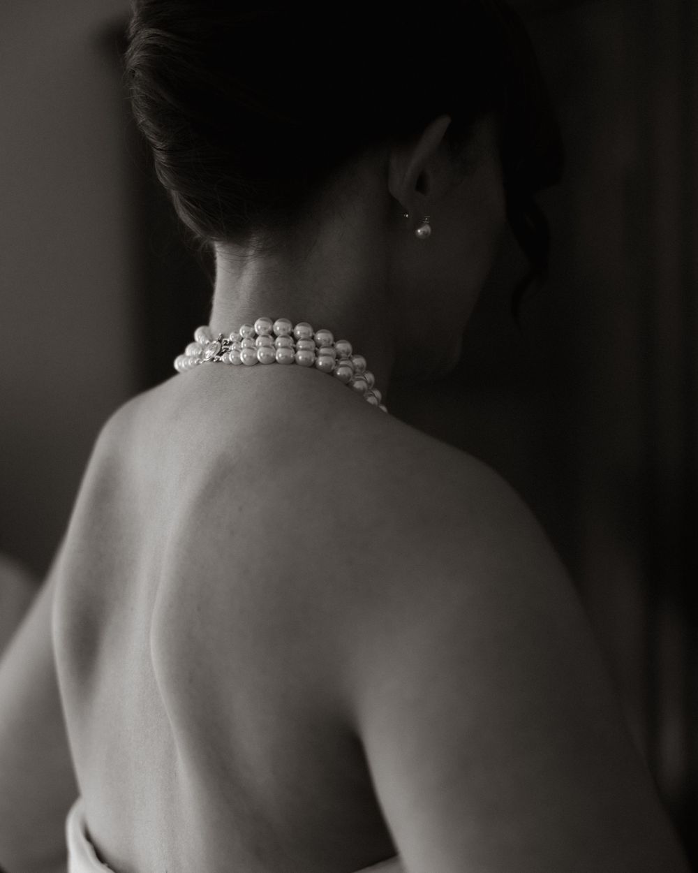 Artistic black and white photo showing bare shoulders adorned with elegant pearl necklace against dark background.