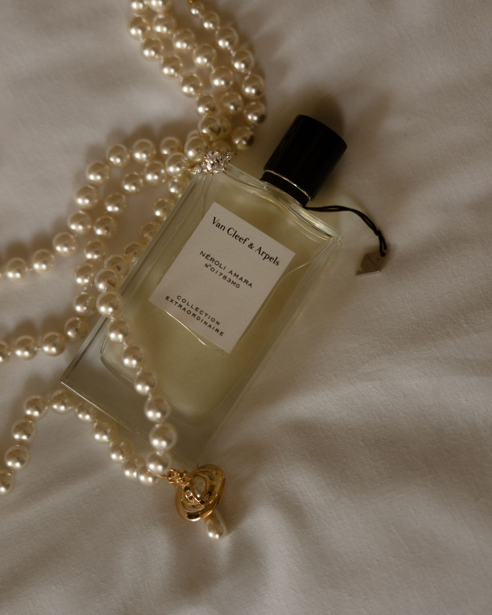 A Van Cleef & Arpels perfume bottle elegantly displayed with a pearl necklace on white fabric.