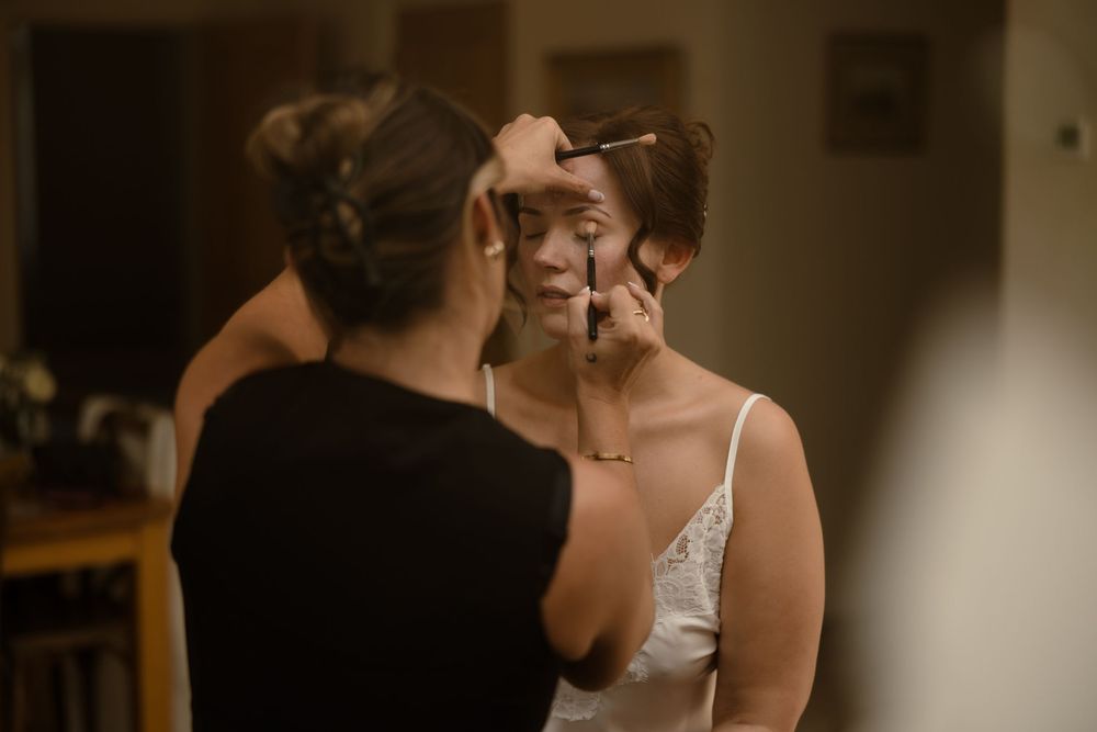 A bride has her makeup professionally applied in warm lighting during wedding preparations.