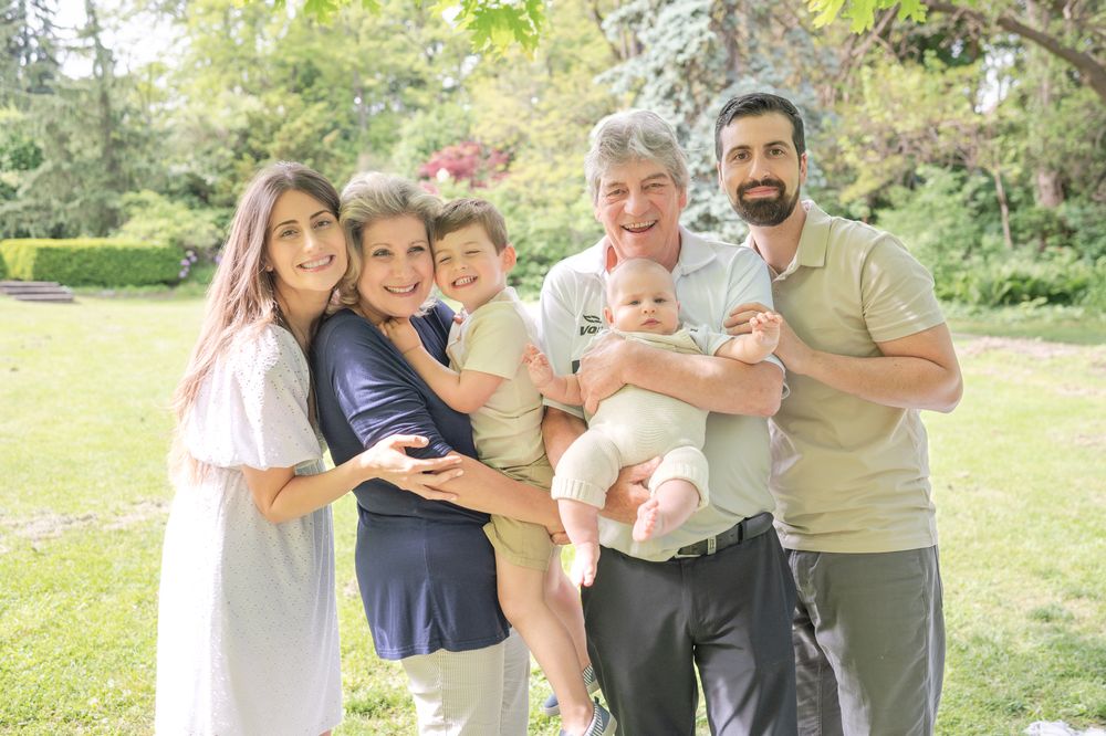 A multi-generational family gathered together outdoors on a sunny day in a lush green garden setting.