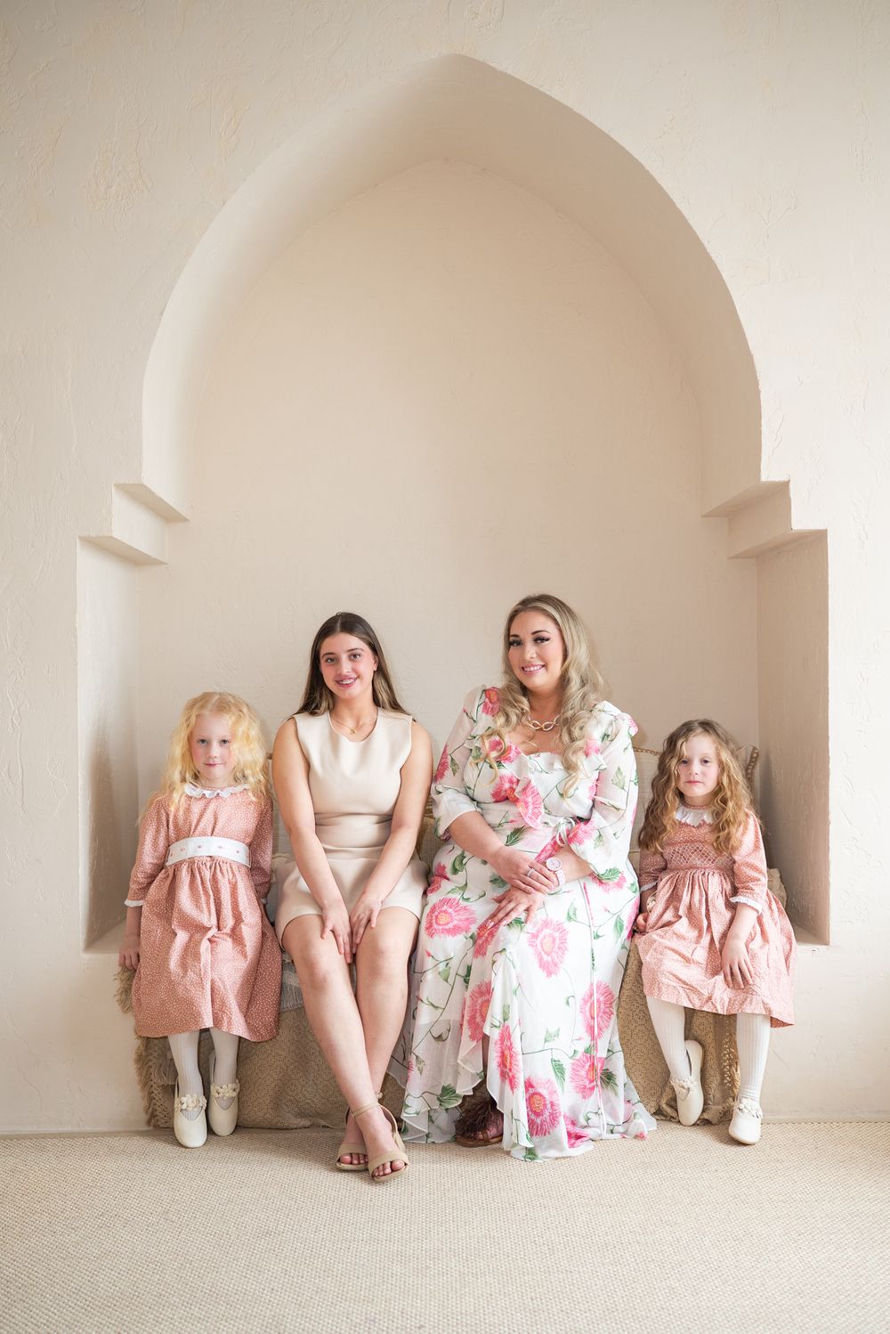 Four people sit together in an arched alcove wearing coordinated pink and white dresses and cowboy boots.