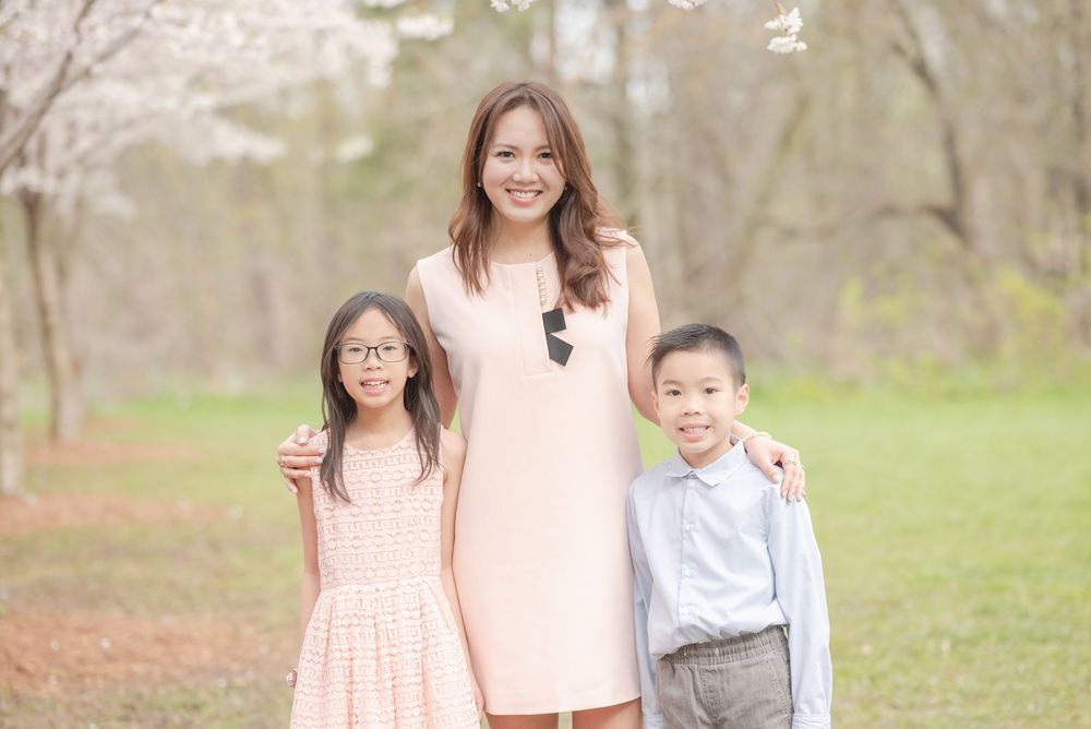 Three people in coordinating pastel outfits pose together outdoors in a springtime garden setting.