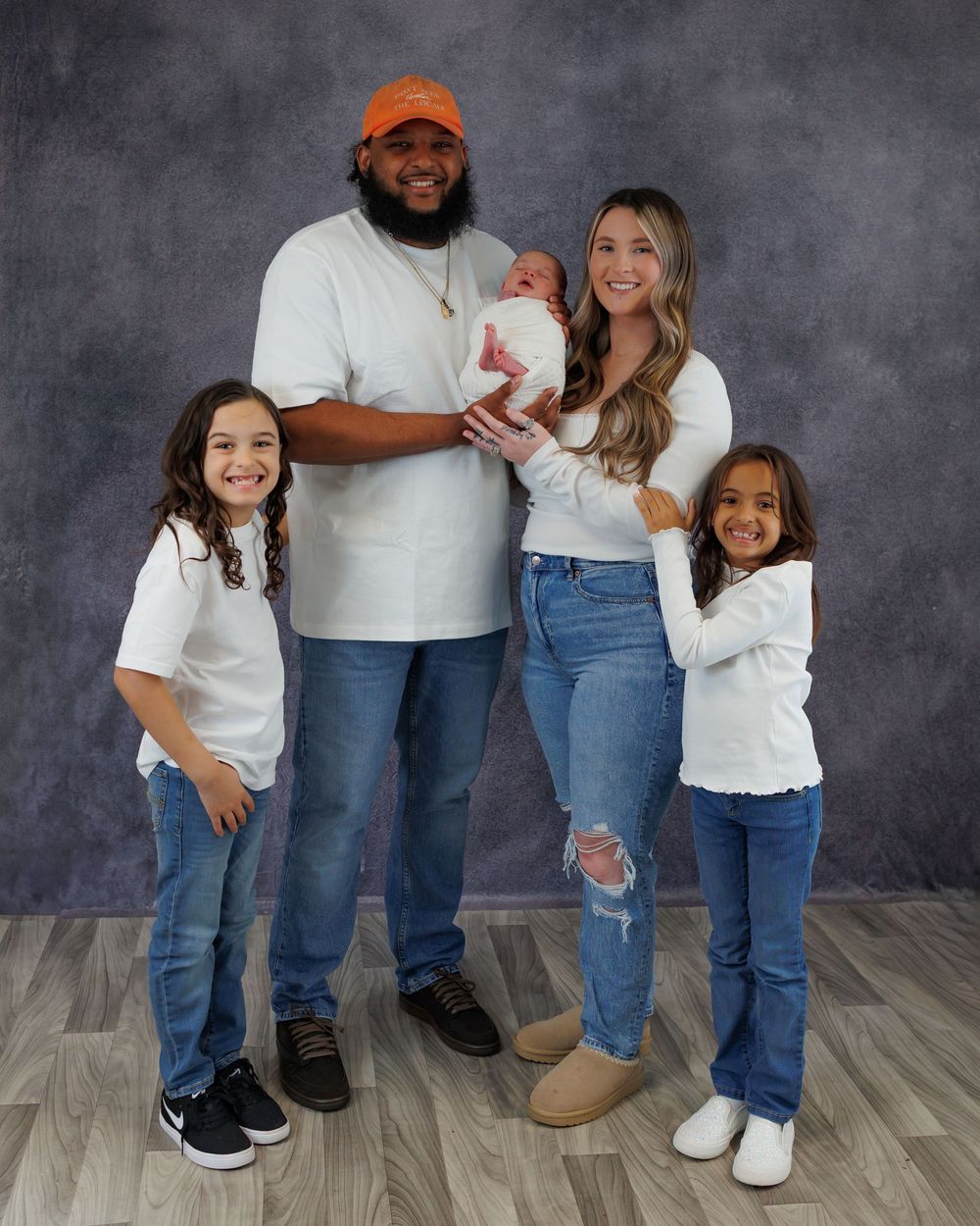 Happy family of five wearing coordinated white shirts and jeans poses together for a portrait against a gray backdrop.