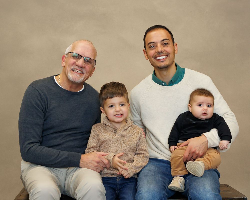Four people sit together in a warm studio portrait against a neutral background.