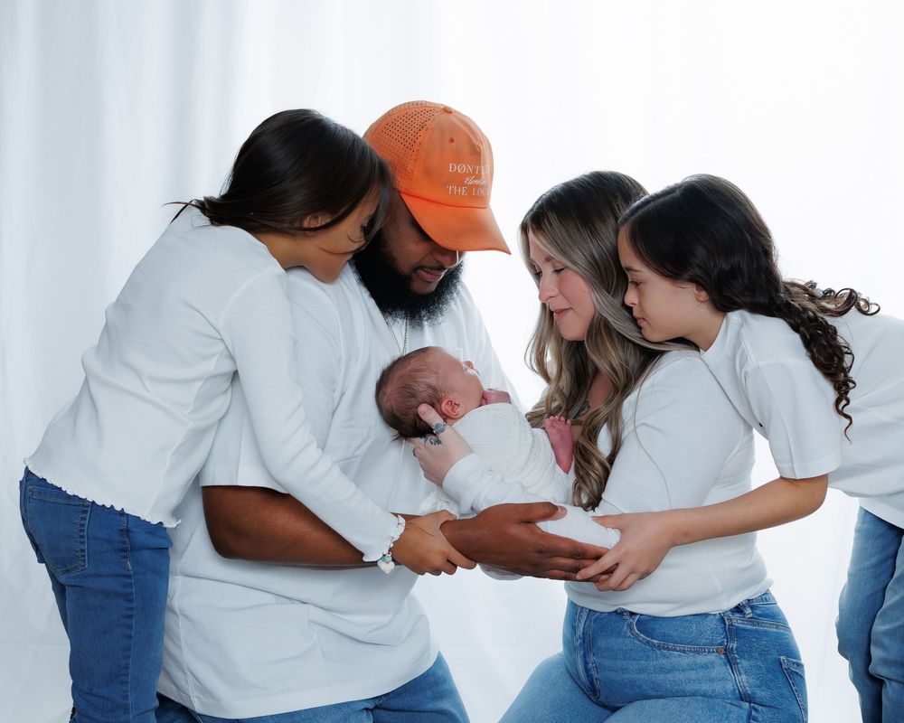 A loving family gathers close together while holding and admiring a newborn baby in white clothing.