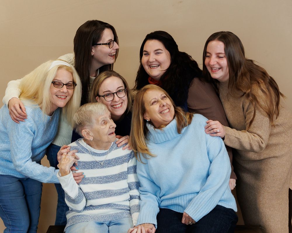 A cheerful group wearing cozy sweaters huddle together for a casual indoor portrait.