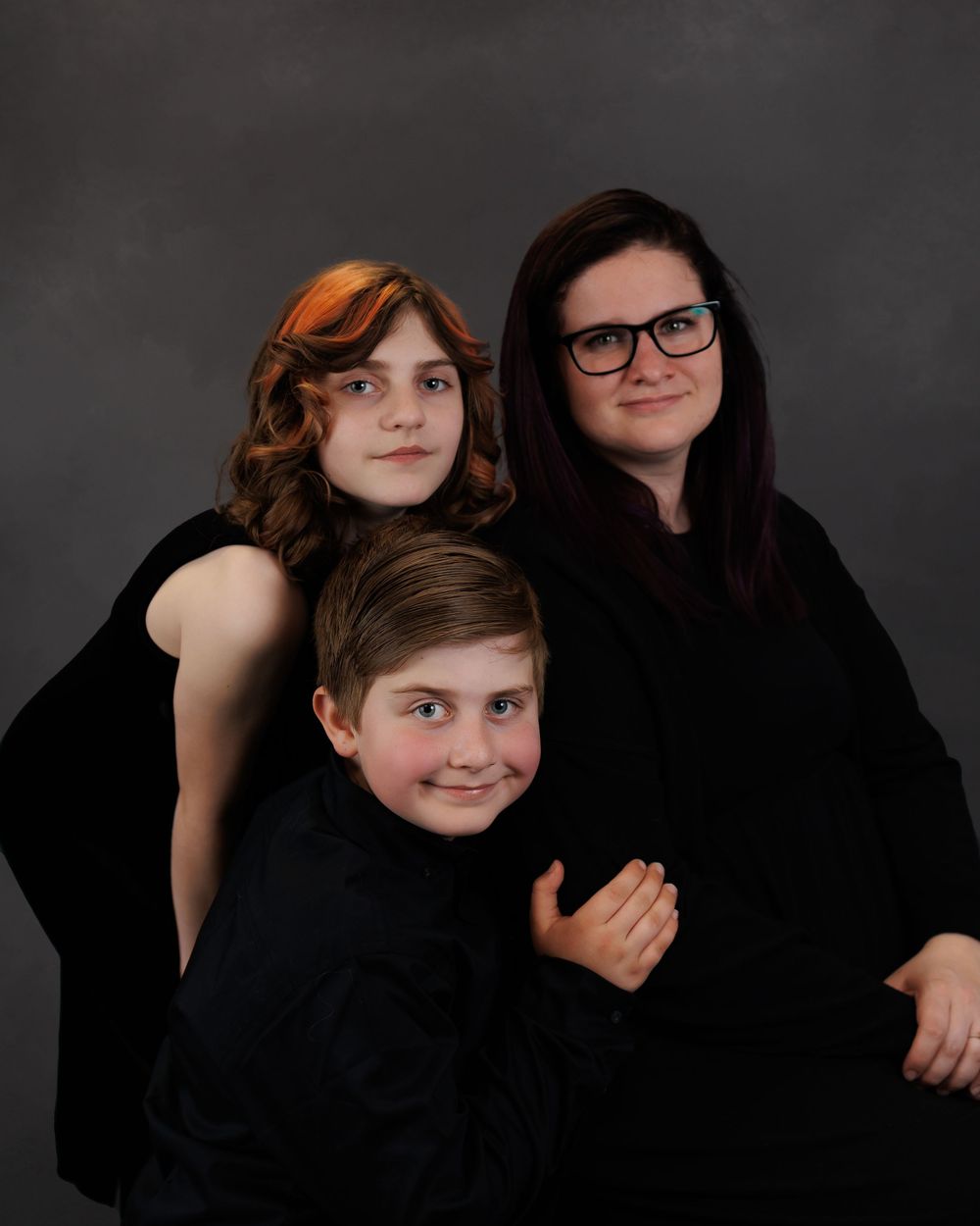 Professional studio portrait of a family wearing black attire against a dark gray background.