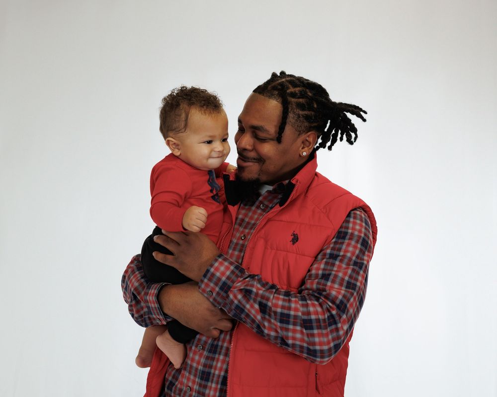 Two people in red attire share a tender familial moment against a white studio backdrop.