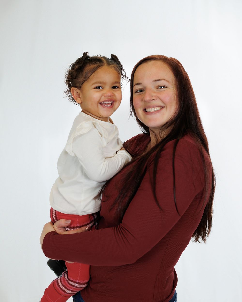 A heartwarming portrait of two people in coordinating burgundy and white outfits sharing smiles against a light background.