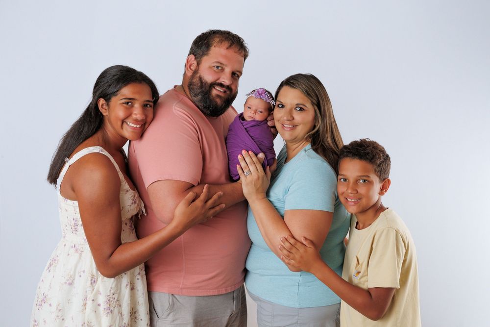 A family poses together against a light gray background wearing summer casual attire.