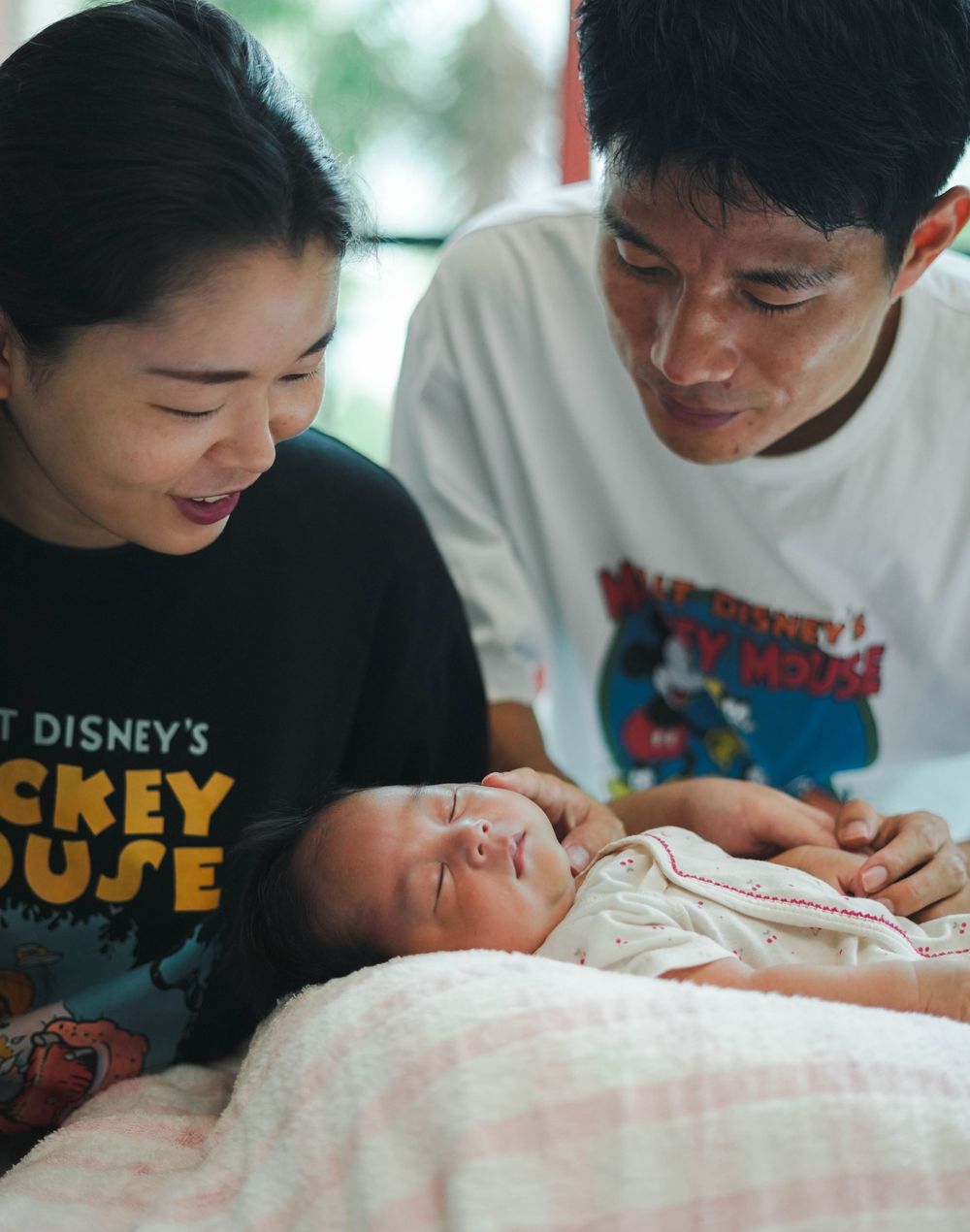 A tender family moment as two people gaze lovingly at a sleeping baby wrapped in soft blankets.