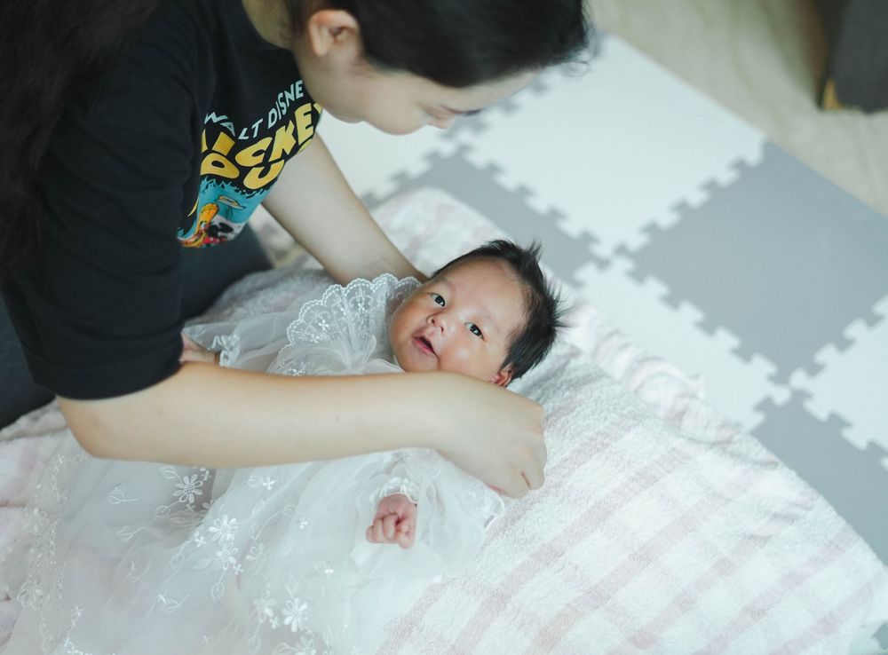 A happy baby lies on a soft white mat while being tended to from above.