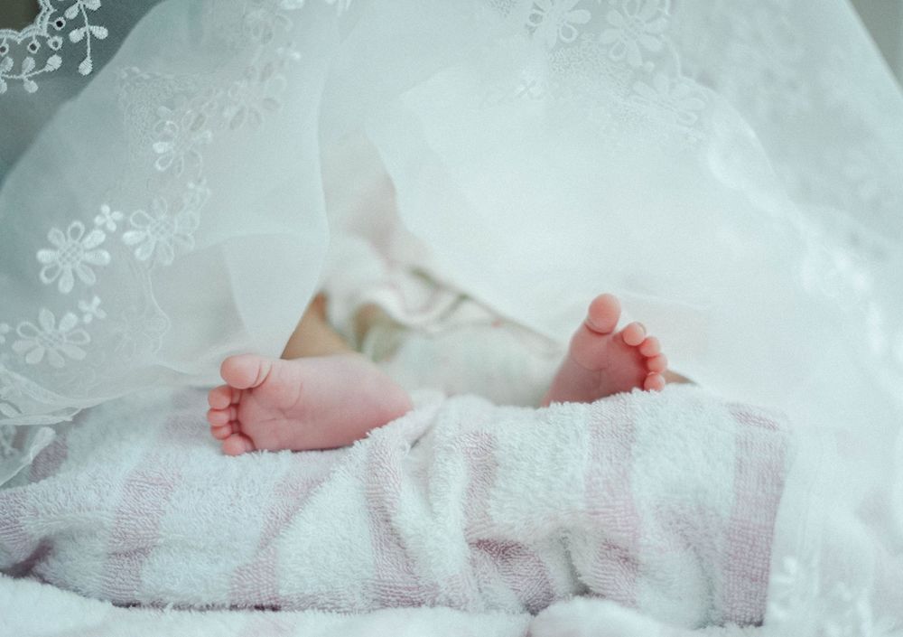 Tiny baby feet peeking out from under delicate white lace and soft blankets in a tranquil nursery setting.
