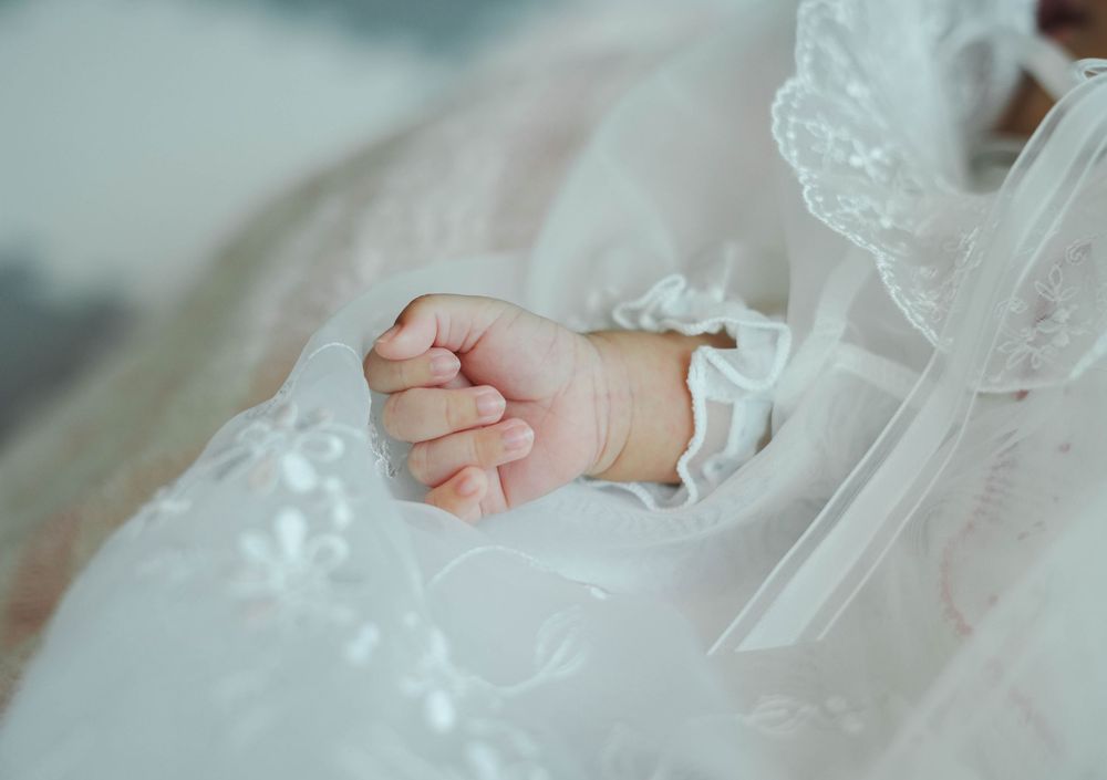 A tiny baby hand rests on delicate white lace fabric, creating a tender moment captured in soft focus.