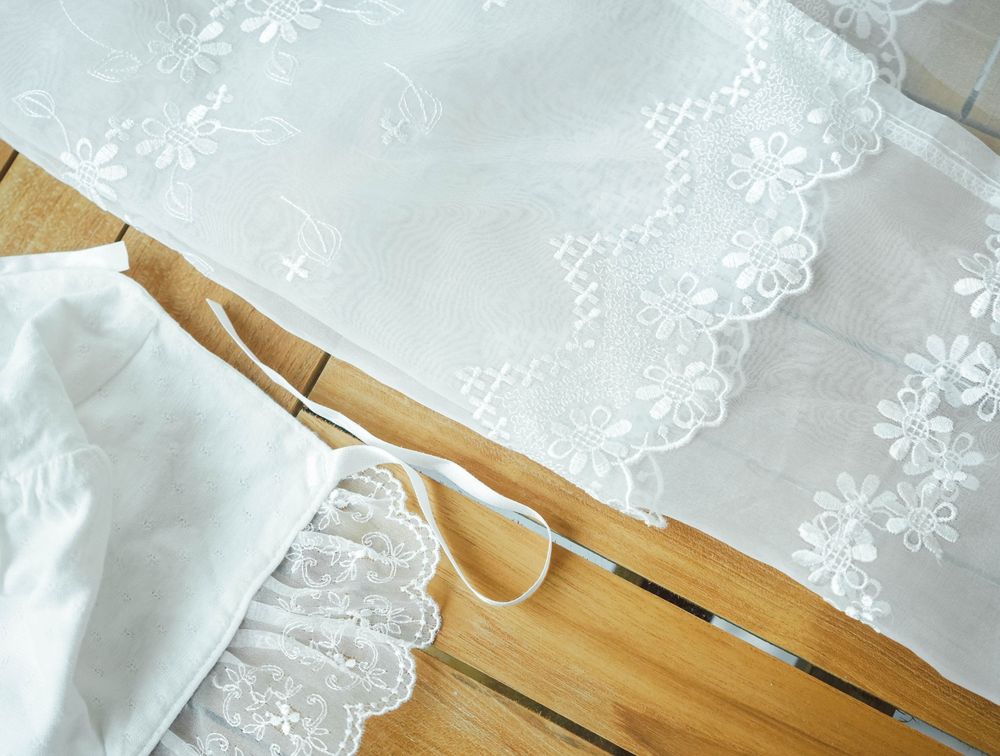 Delicate white lace trim details on sheer fabric displayed against a wooden surface.