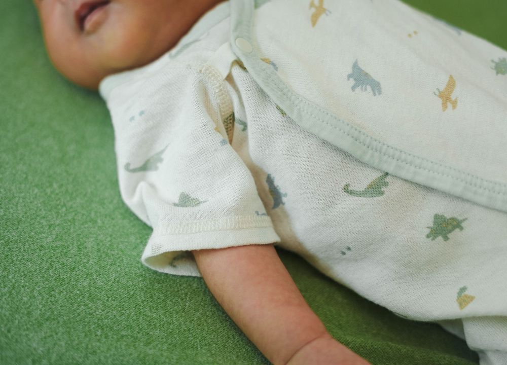 Baby wearing white pajamas with dinosaur print design lying on green textured background.