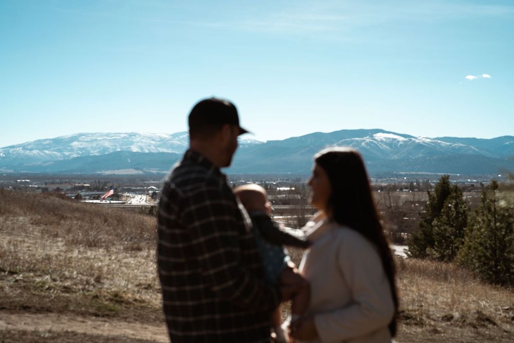 Two people stand together on a hilltop overlooking a scenic mountain landscape on a clear sunny day.