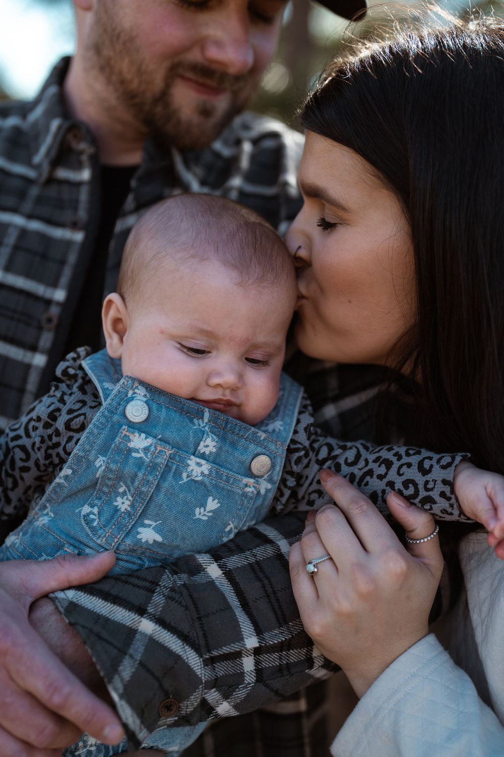 A family shares an intimate moment together while holding their young baby wearing denim in soft lighting.