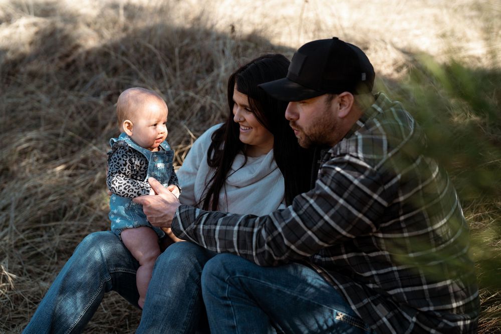 A family dressed in casual clothing sits together outdoors during a candid moment in natural lighting.