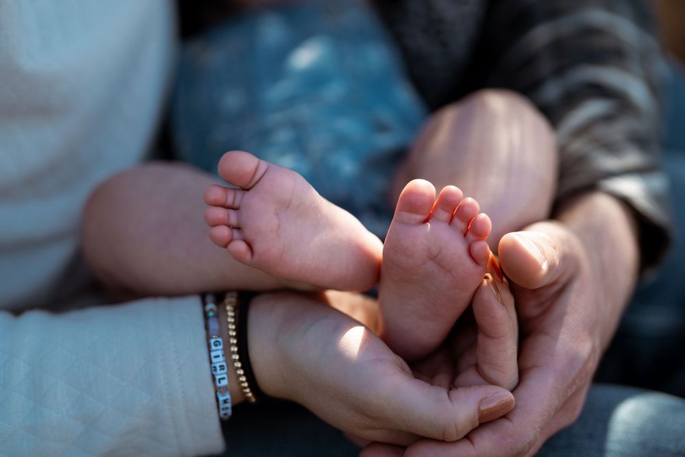 Tiny bare baby feet held gently in adult hands with soft natural lighting streaming across the scene.