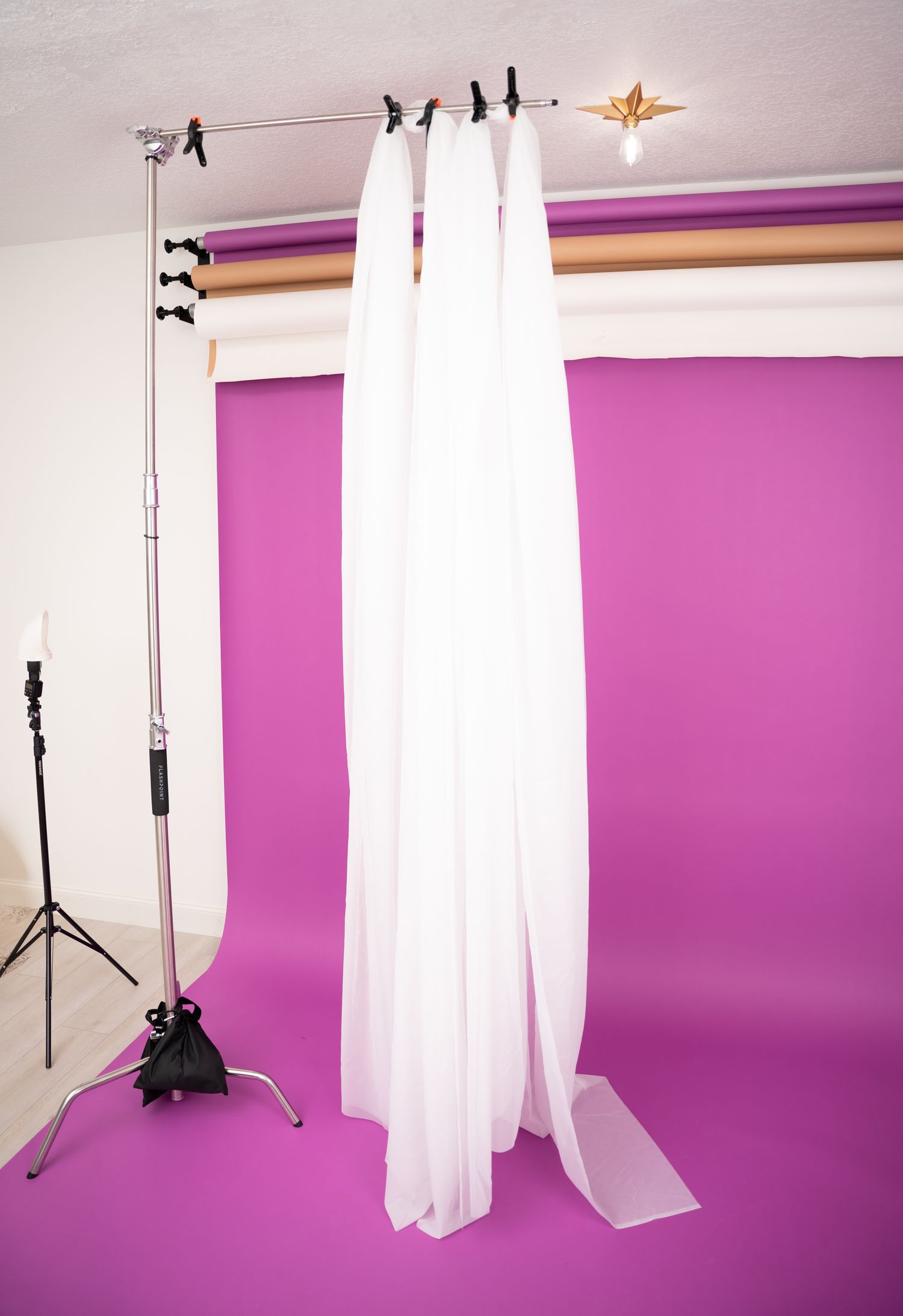 Photography studio setup with white curtains and lighting equipment against purple backdrop.