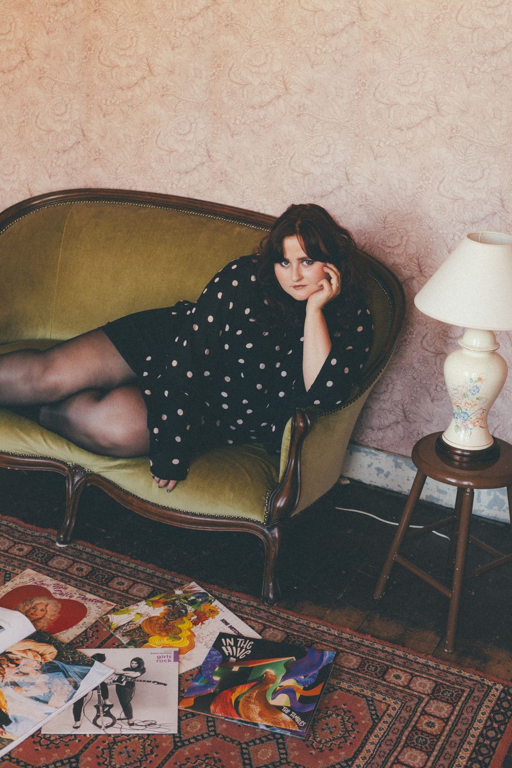 A vintage-inspired indoor photoshoot with a black polka dot dress on a yellow velvet couch with scattered photos below.