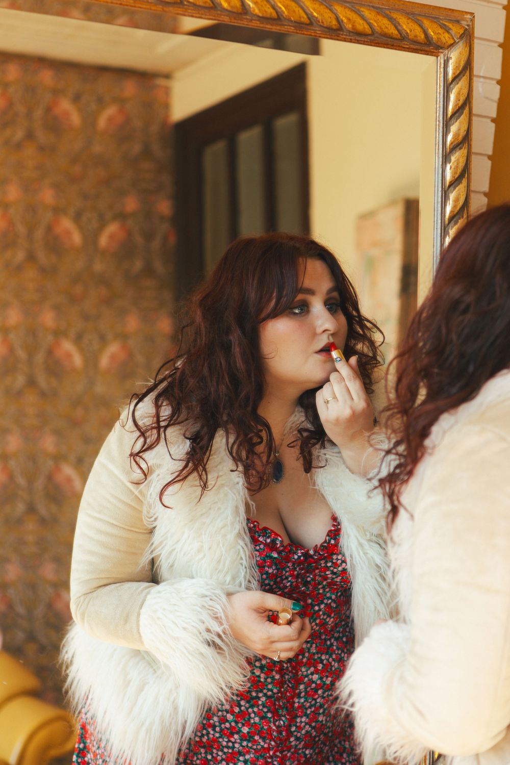 A mirror reflection shows a vintage-style look featuring a white furry jacket and floral dress.