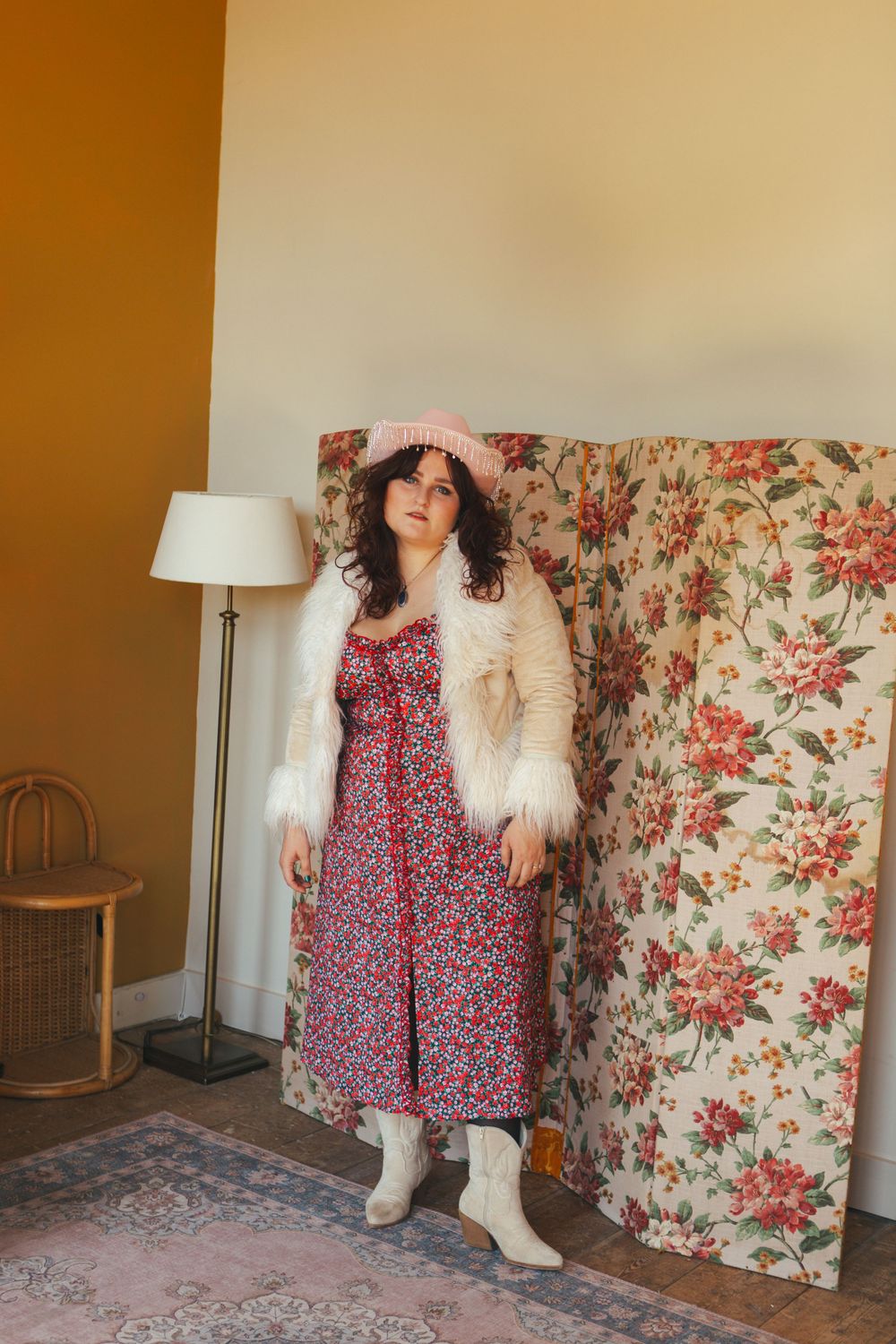 Fashion photoshoot featuring a floral dress paired with a white fluffy coat against a floral wallpaper backdrop.