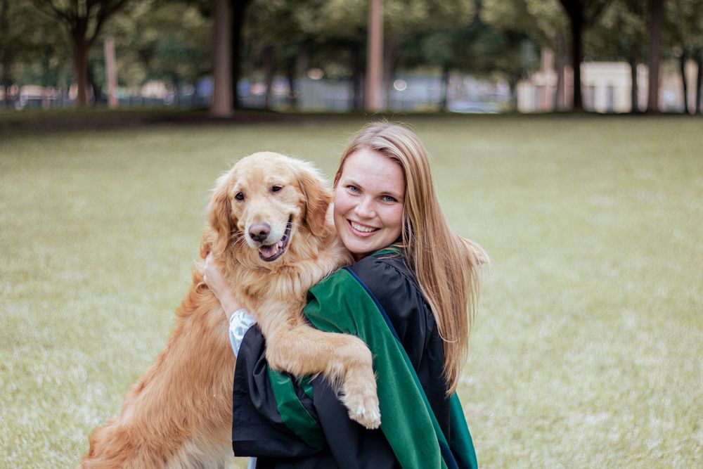 A person in green hugging a happy golden retriever on a grassy lawn in a park setting.