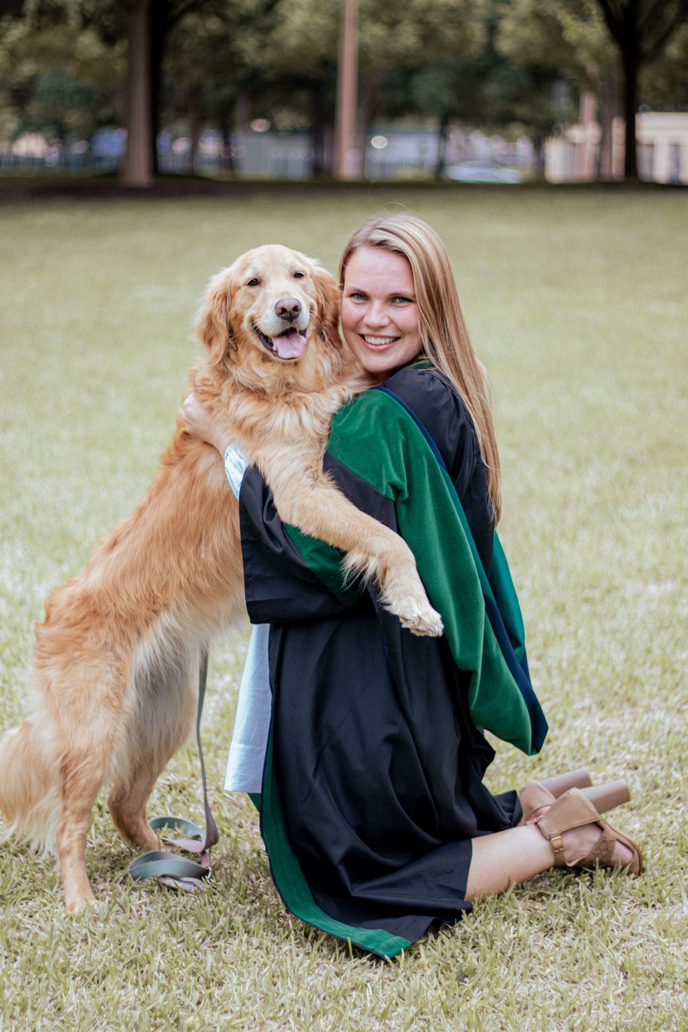 A Golden Retriever poses with someone in graduation regalia on a grassy lawn during a celebratory photoshoot.