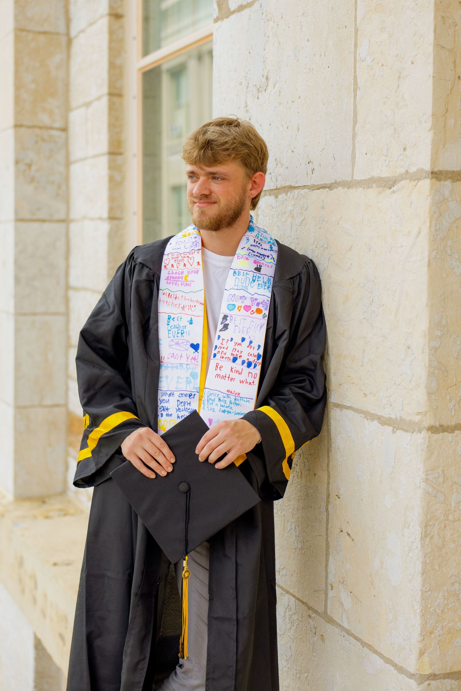 A portrait of a man leaning against a wall in graduation regalia