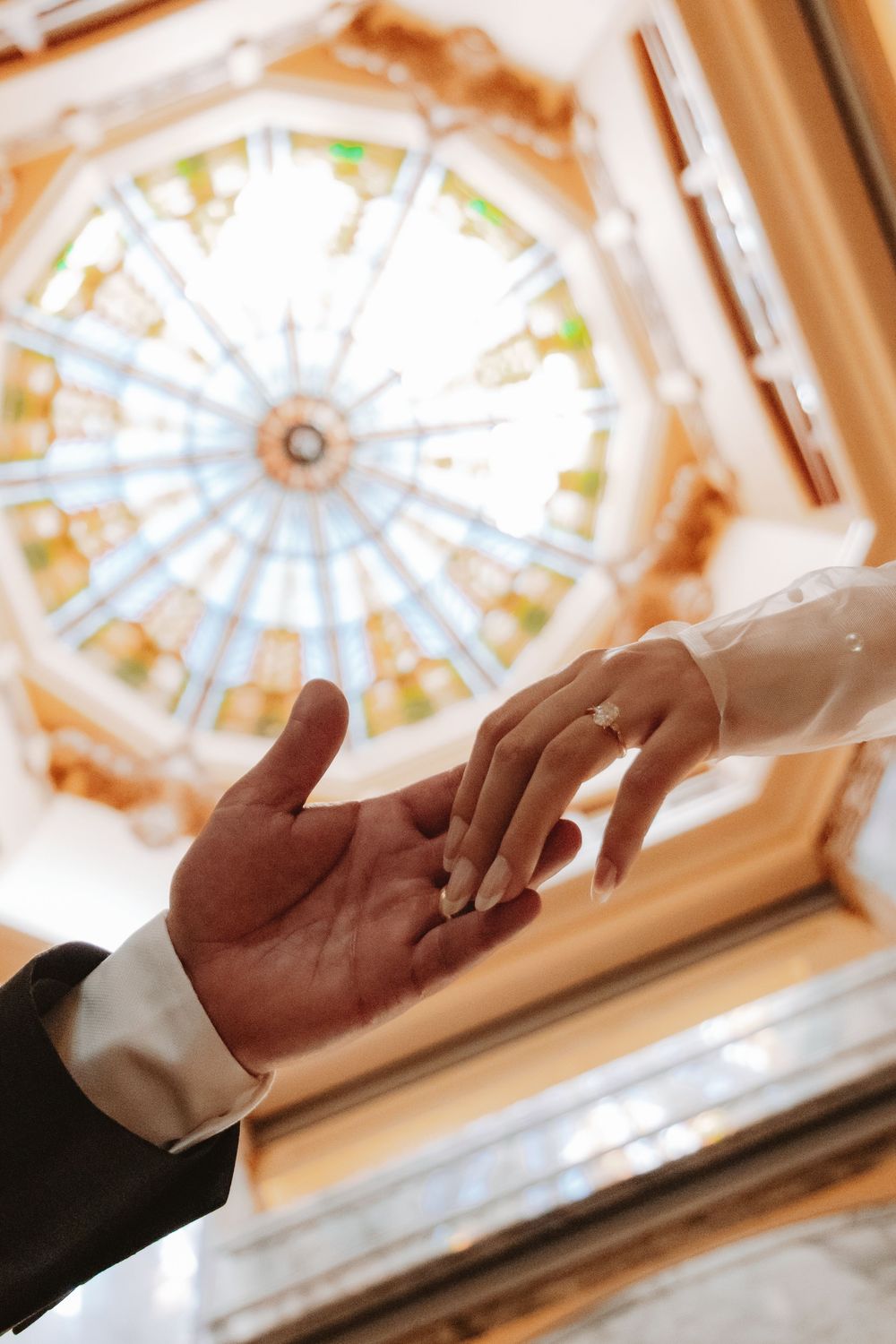 Wedding detail shot of the bride and grooms hands from below enhancing the stained glass window above them at the Harris County Courthouse.