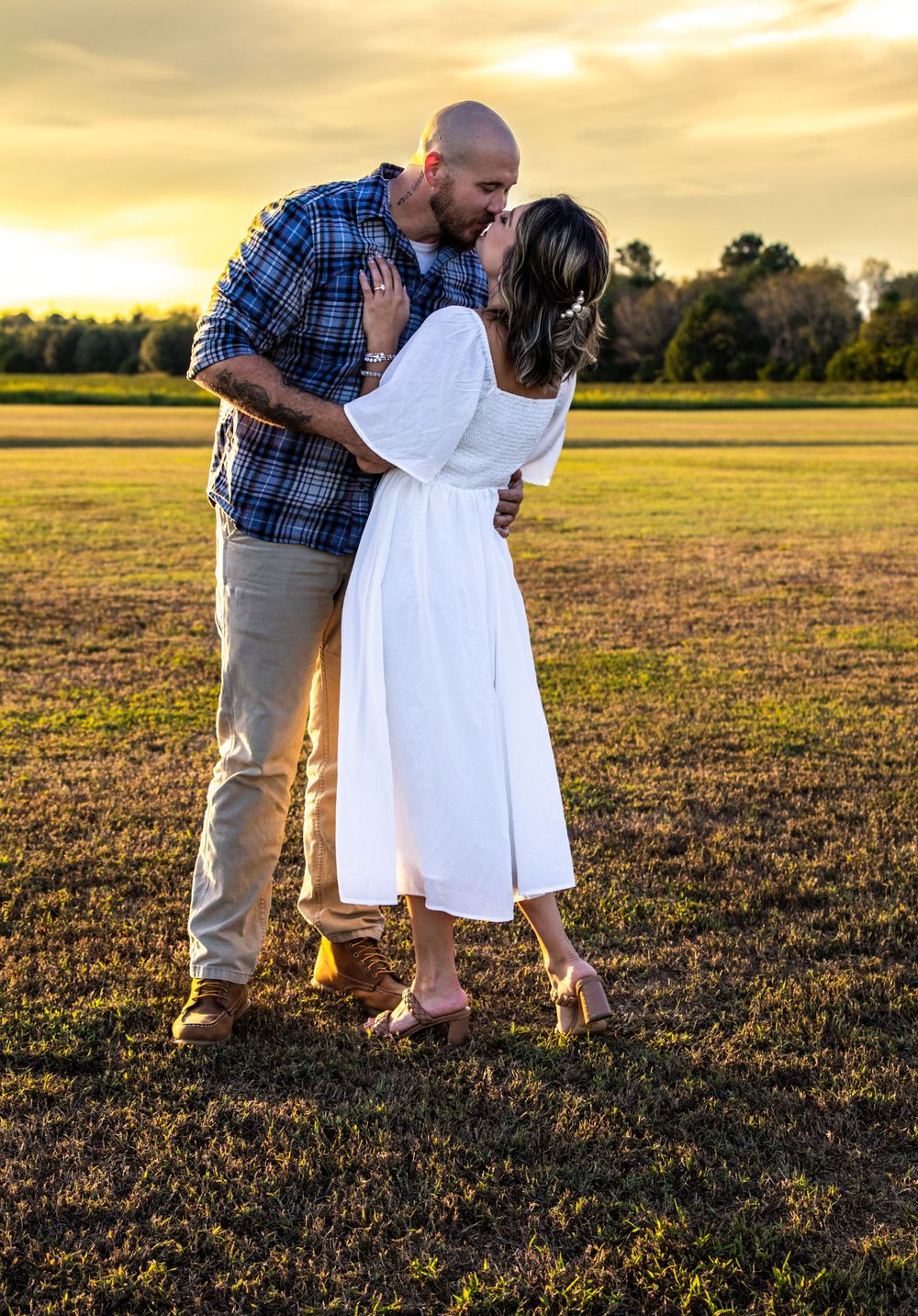 Couple sharing a kiss in an open field bathed in warm golden sunset light.