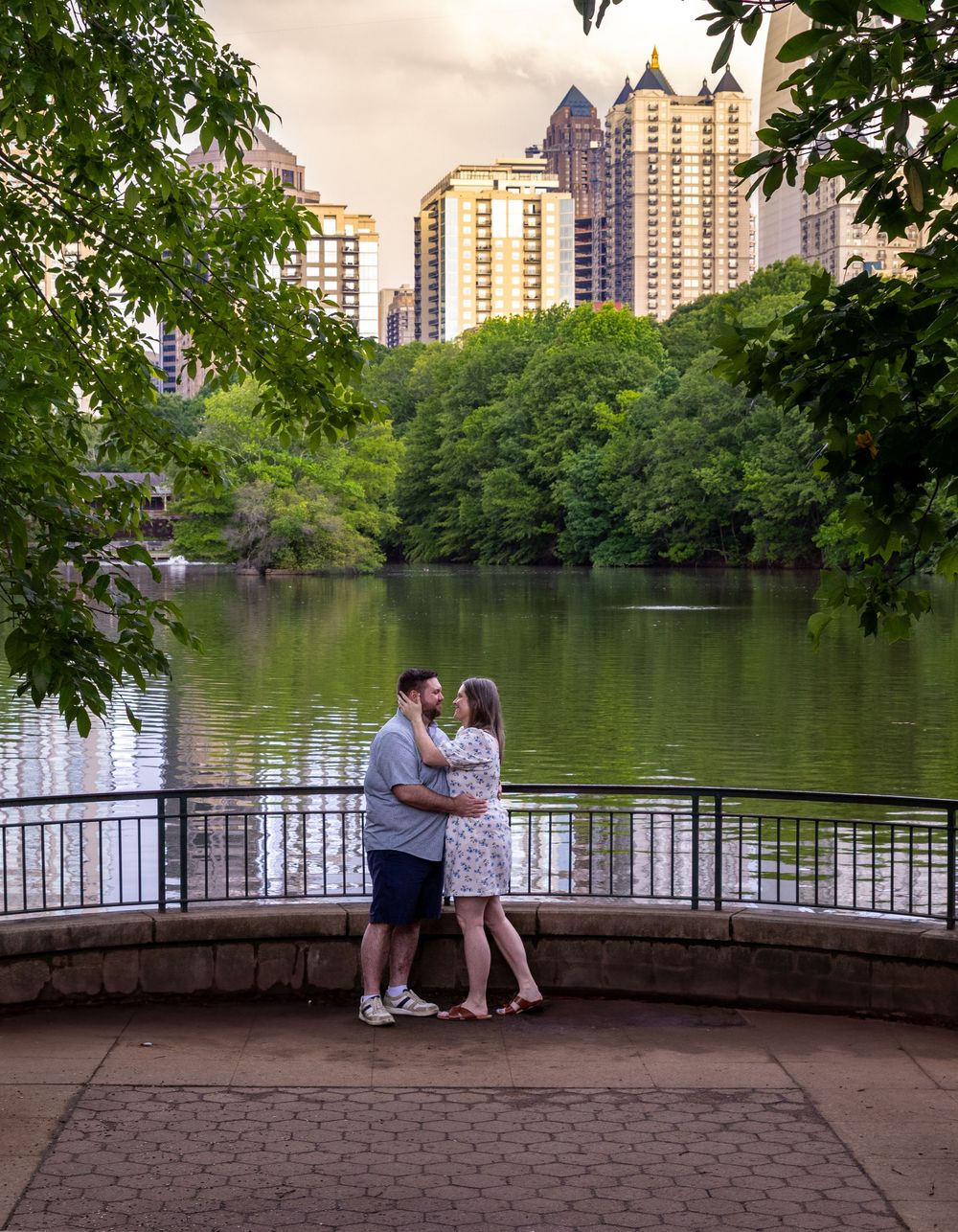 Romantic couple embracing by a lakeside railing with Atlanta city skyline glowing at golden hour.