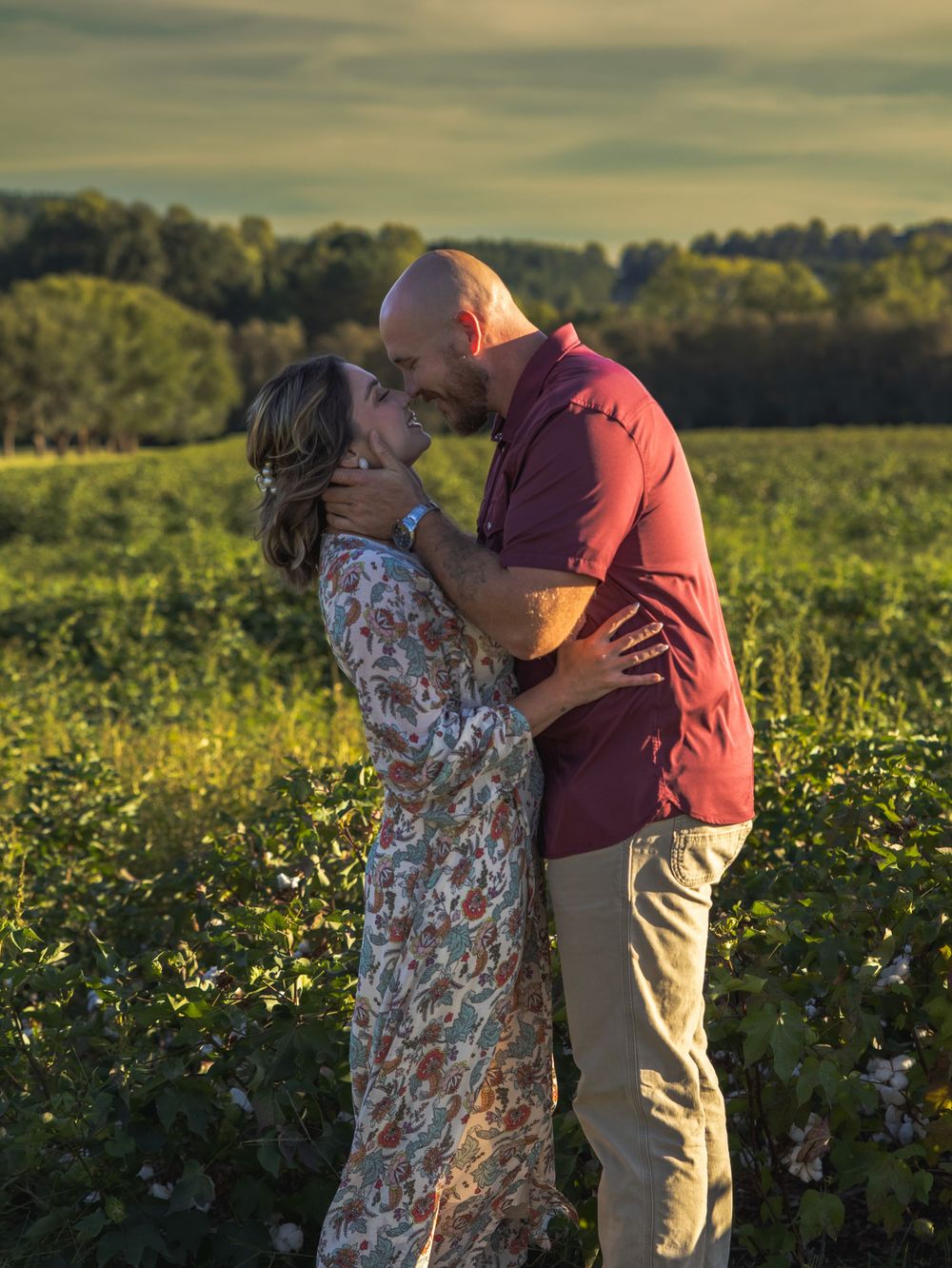 Couple sharing a kiss in a blooming green field during warm golden hour sunlight.