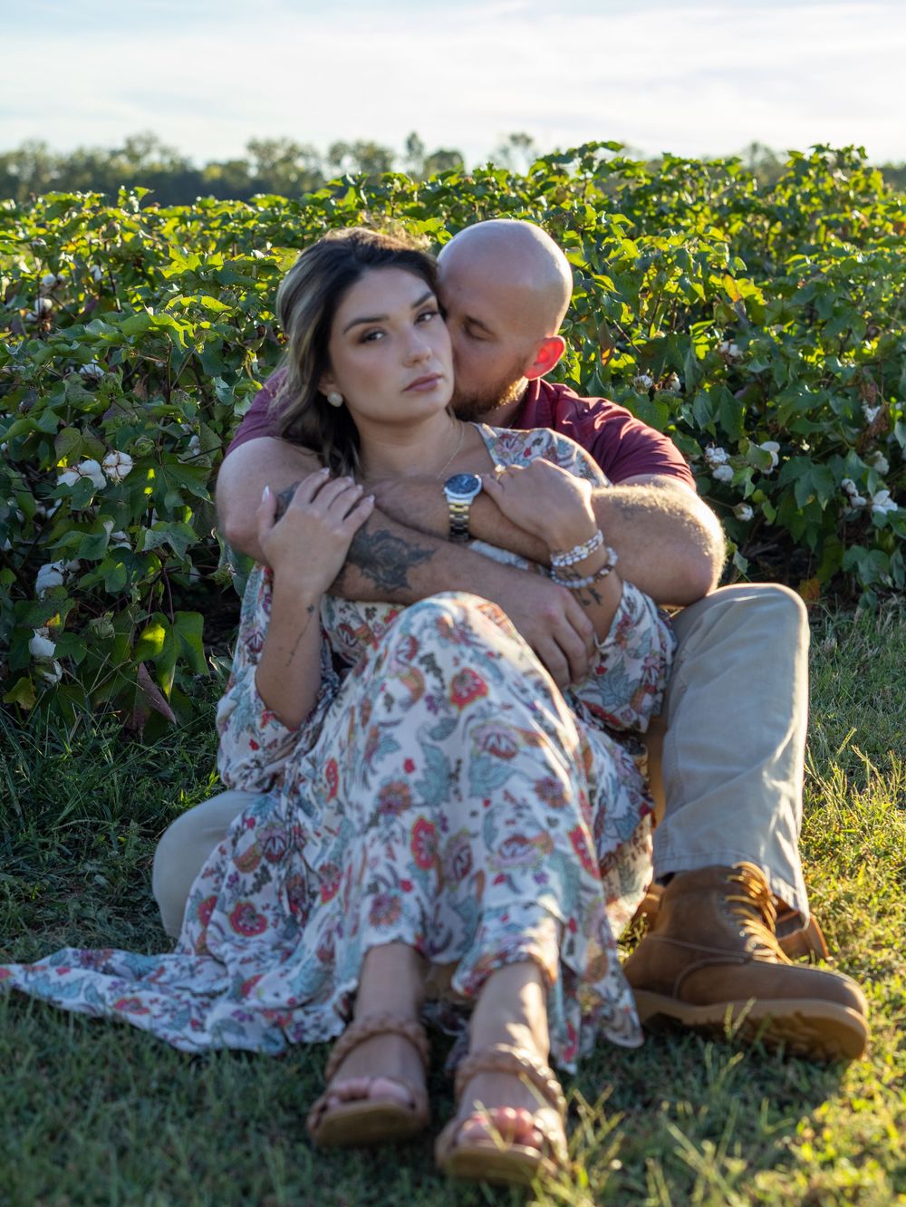 A couple sits intimately together in a lush green vineyard field during golden hour.