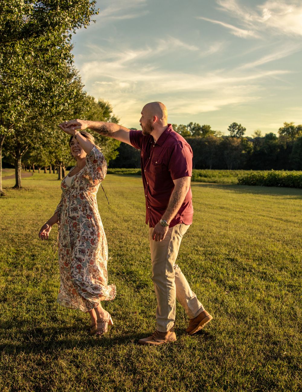 A couple dances and twirls together in a sunlit green park during golden hour.
