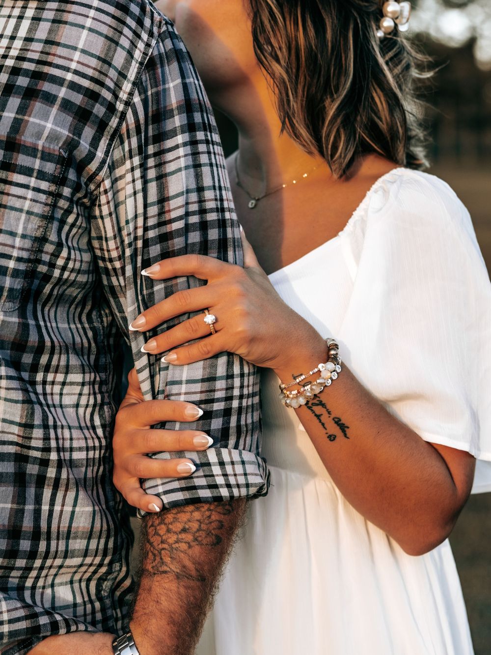 Close-up of a couple embracing, woman in white dress with bracelets and ring, man in plaid shirt with tattoo sleeve.
