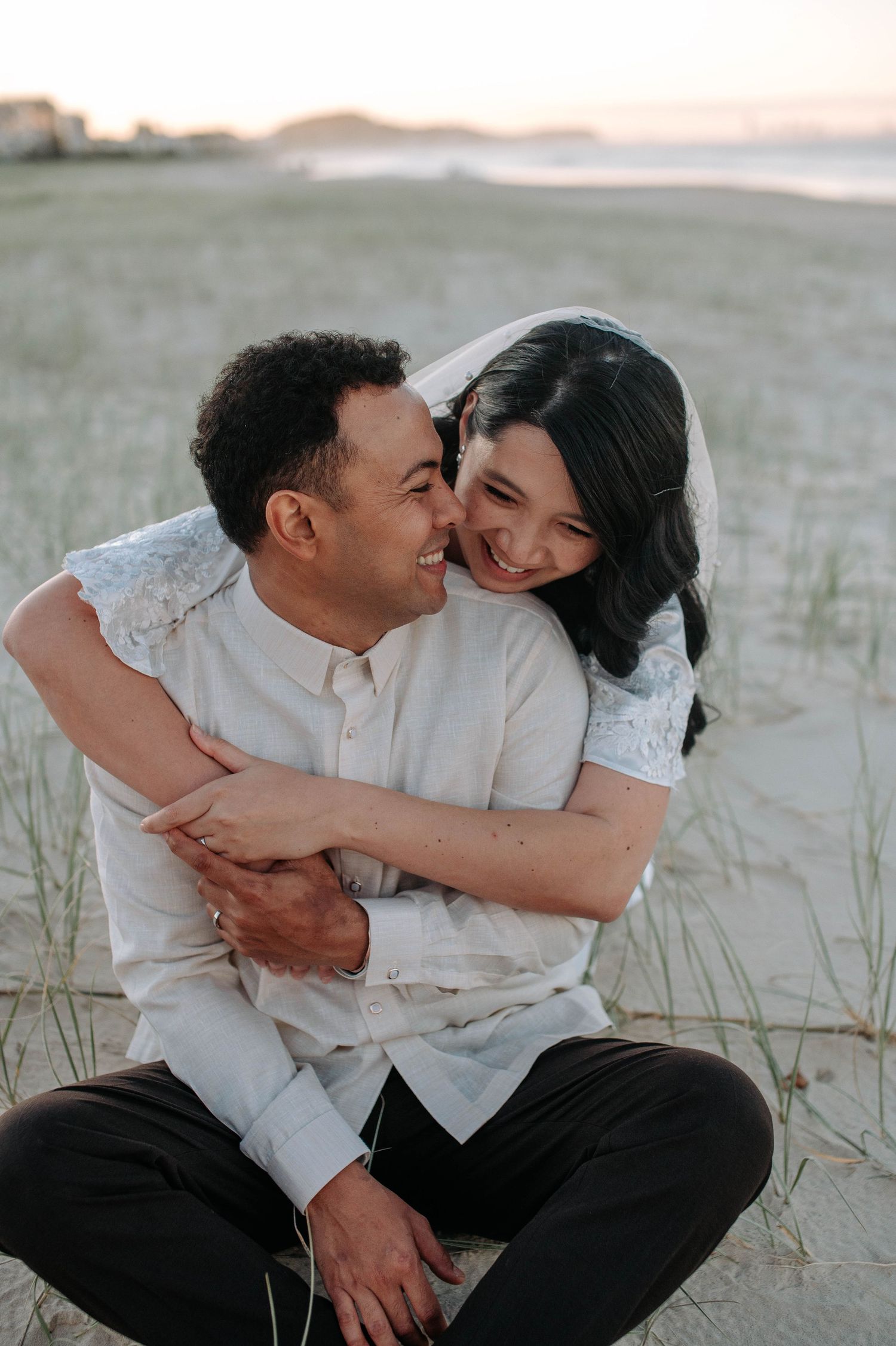 A loving couple embraces and laughs together on a sandy beach during sunset.