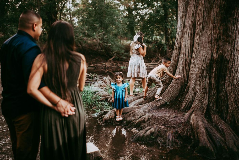 Kids exploring the outdoor river and trees while parents hold hands and watch them in San Antonio Texas.