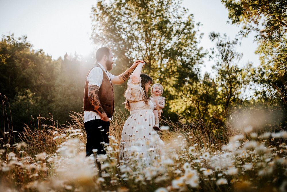 Family of three dancing in a field of flowers with the sunsetting behind the trees in Portland, Oregon.