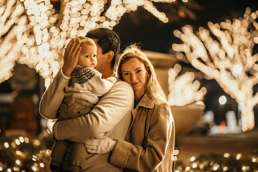 Family of three in downtown, Clarksville, Tennessee with the Christmas lights wrapped around the trees in the background.