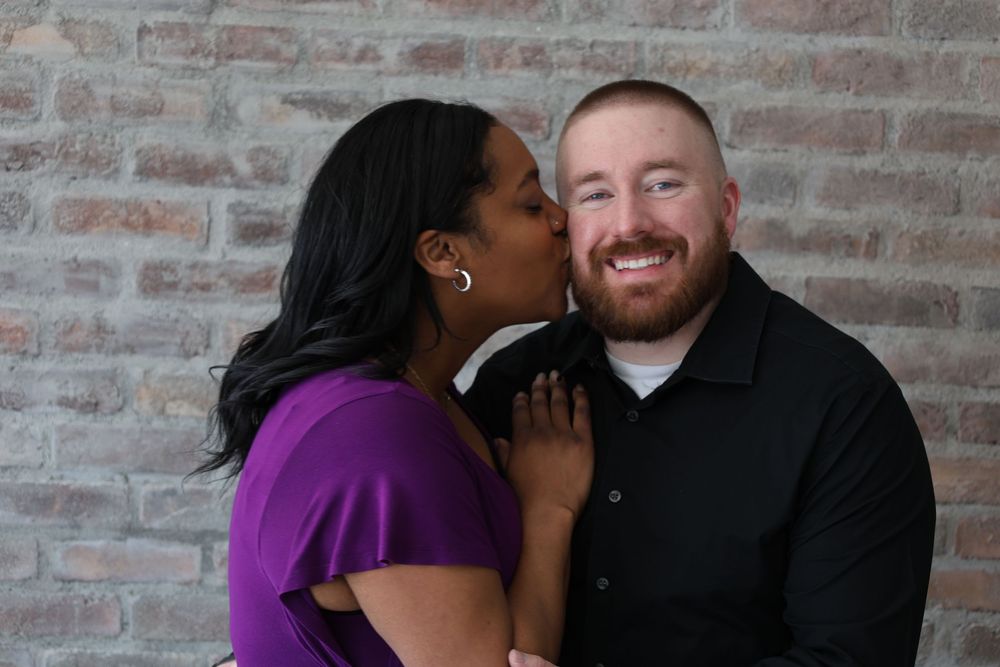 A couple shares a sweet candid moment together against a rustic brick wall background.
