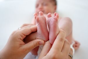 Adult hands gently massage tiny feet of infant lying on white blanket during tender parenting moment.