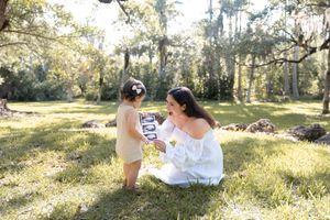 A tender moment shared between two people on a sunlit grassy lawn with mossy oak trees in the background.