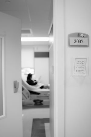 Black and white view through doorway into hospital room 3037 showing silhouette of patient in bed.