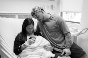 A tender family moment captured in black and white as parents gaze lovingly at their newborn baby in a hospital room.